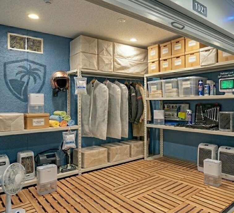 沖縄特有の湿気から荷物を守るため、那覇市のトランクルームで具体的な対策を行う日本人女性。木製のすのこを敷き、壁から隙間を開け、除湿剤や不織布を活用してカビを防いでいる